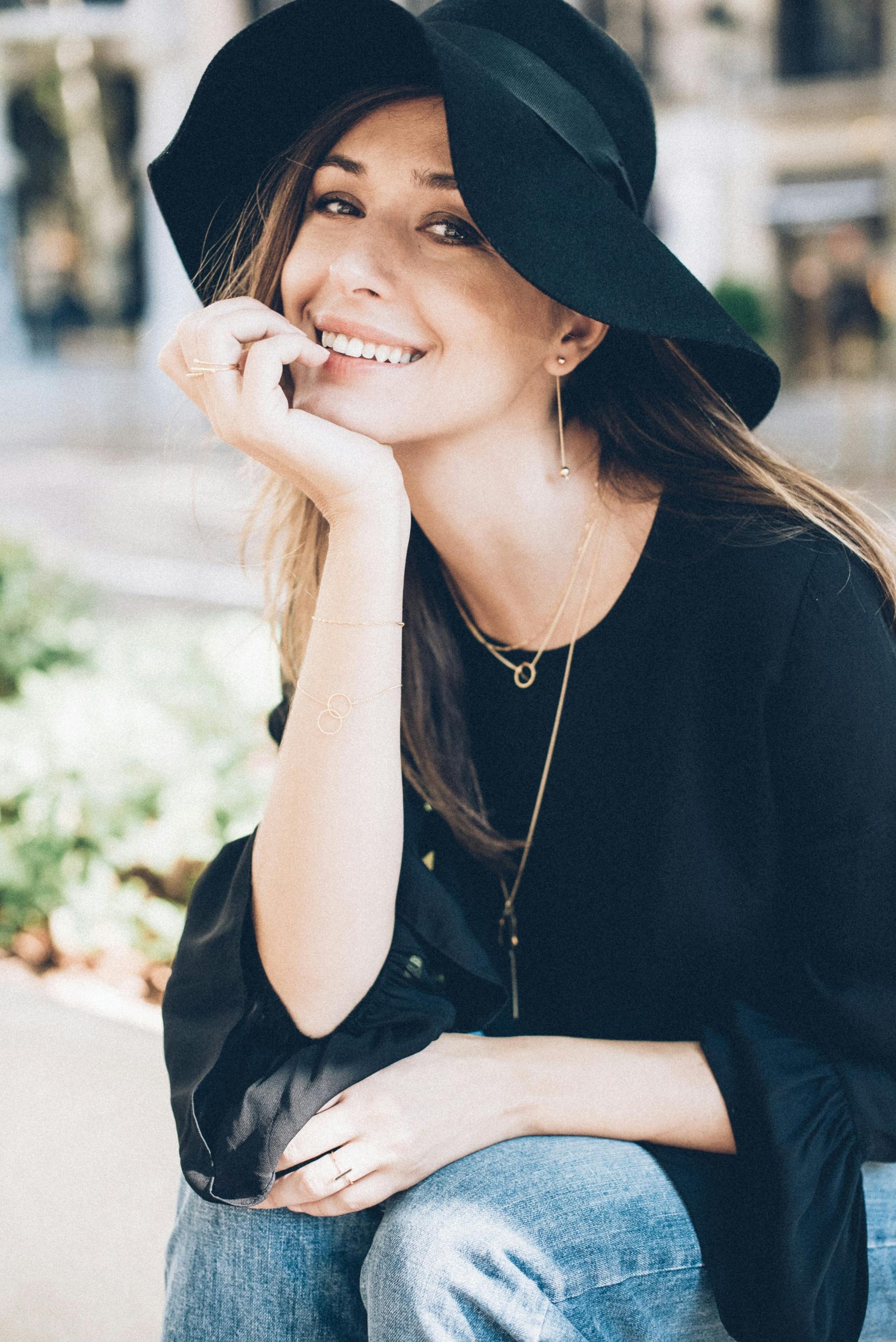 Charming woman in black hat and blouse smiling outdoors, embodying casual elegance.